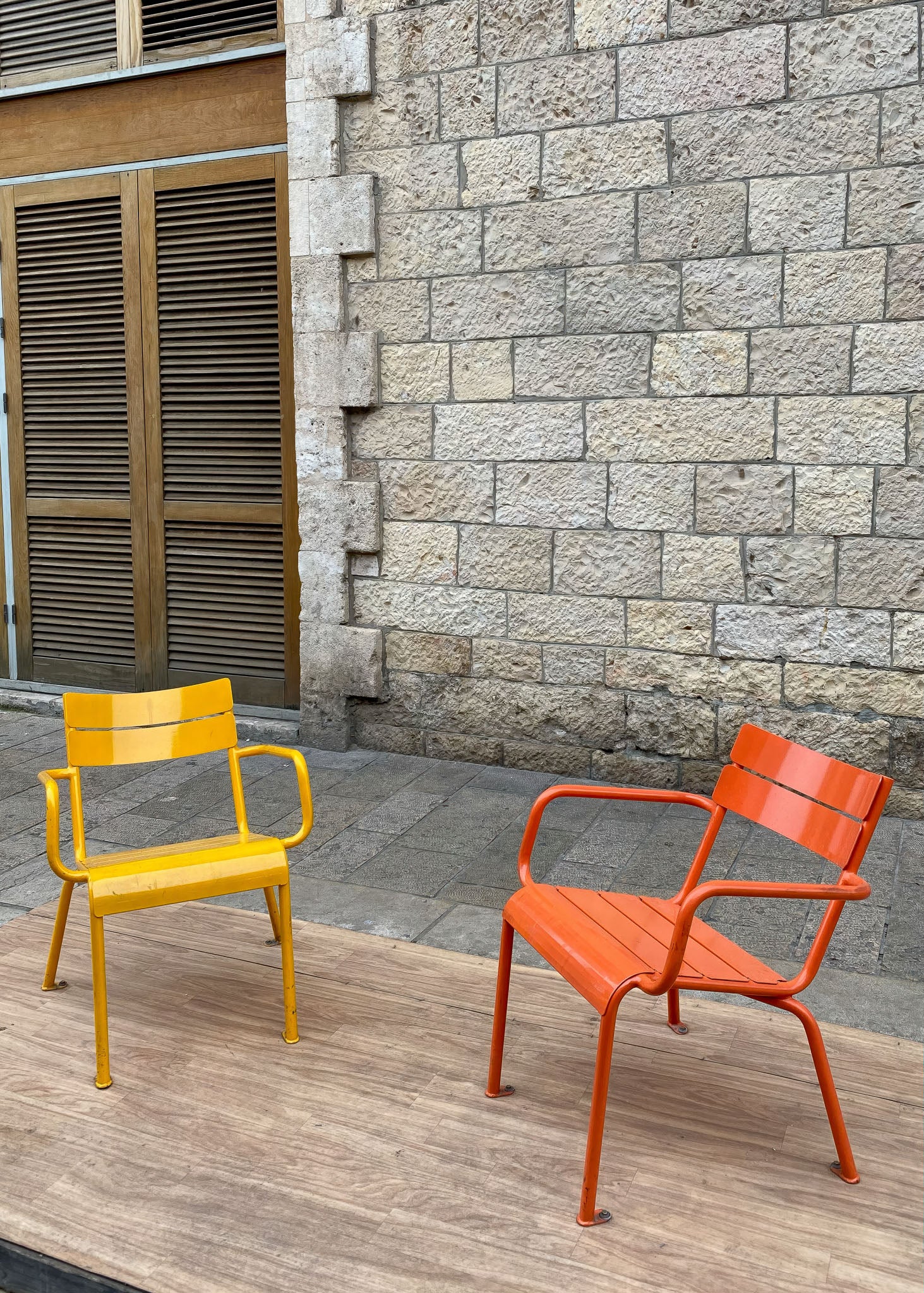 Printed Poster featuring vibrant yellow and orange chairs against a stone wall backdrop.