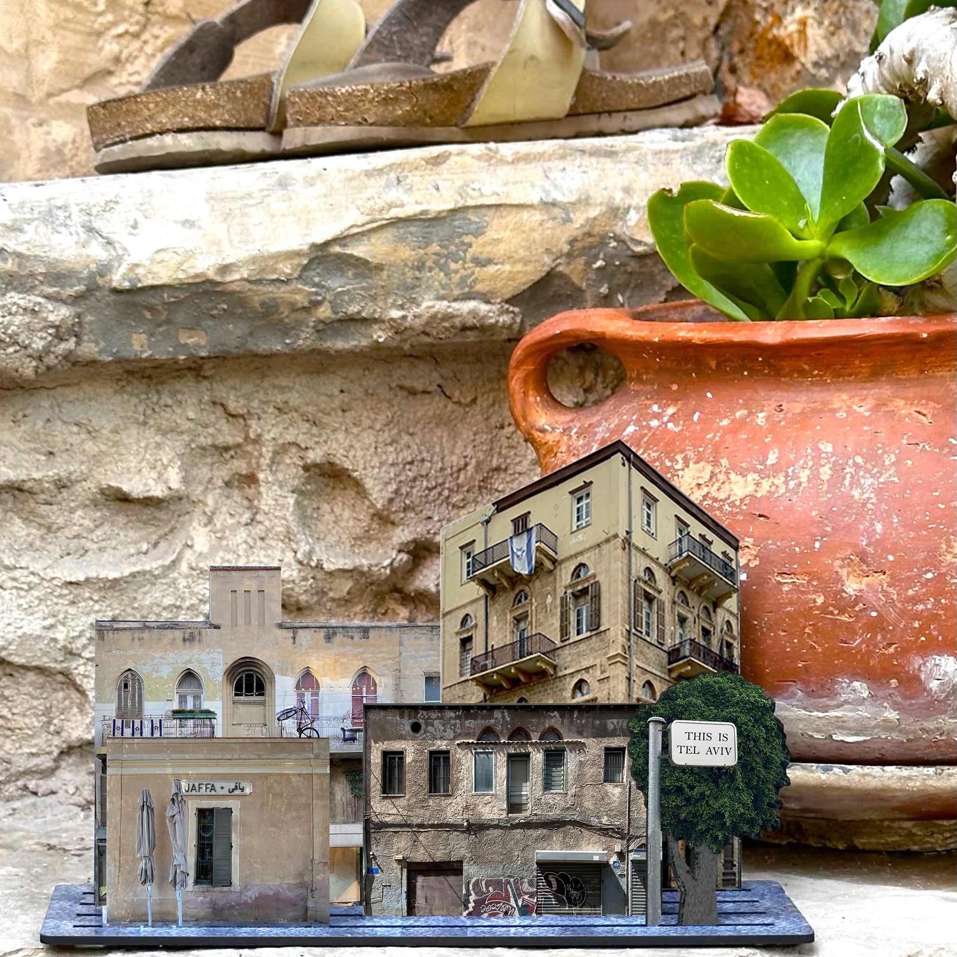THIS IS TEL AVIV Israel Souvenir — City Miniature set displayed on stone steps among plants and sandals.