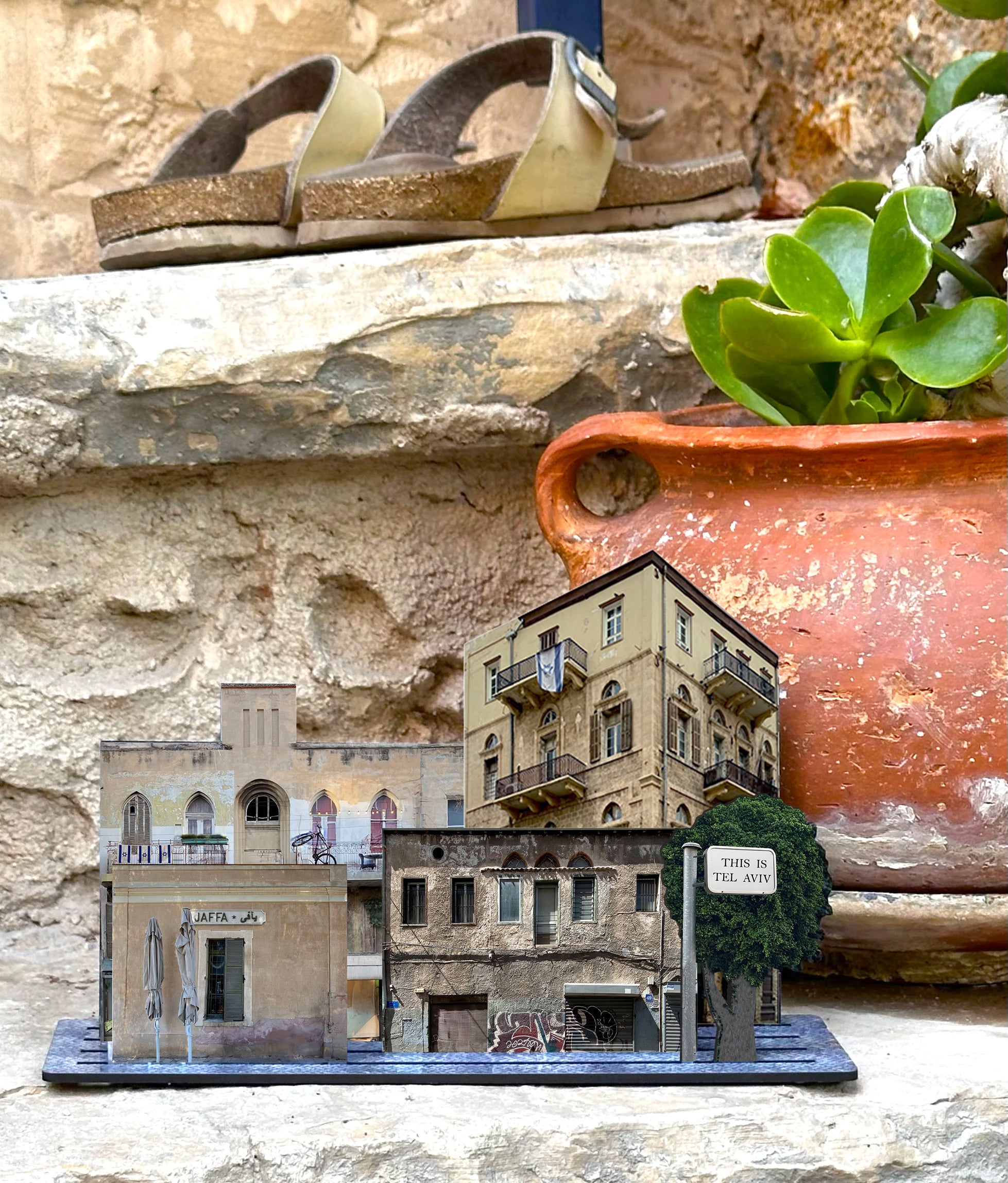 THIS IS TEL AVIV Israel Souvenir — City Miniature set displayed on stone steps among plants and sandals.