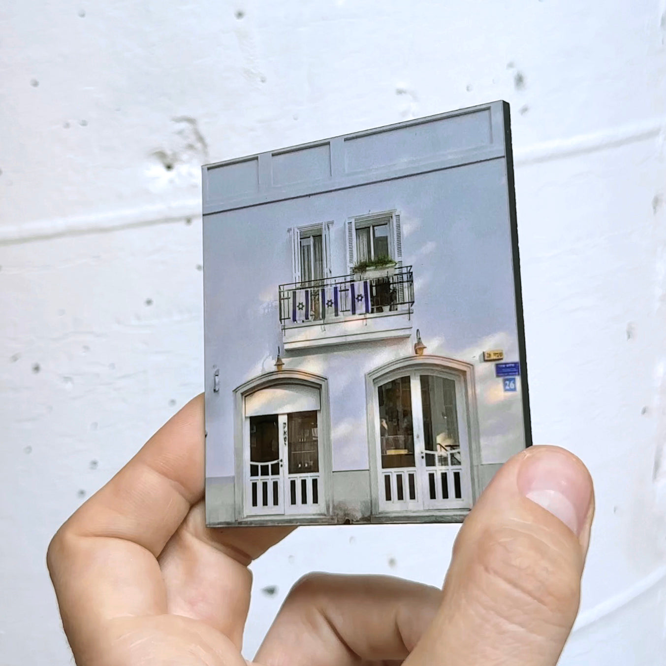 Hand holding a miniature of a Tel Aviv building, showcasing its white façade and balcony, representing THIS IS TEL AVIV Israel Souvenir — City Miniature.